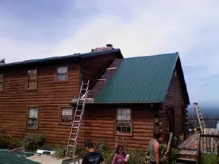 Green metal roof going on a two story log home with ladders set in Jasper